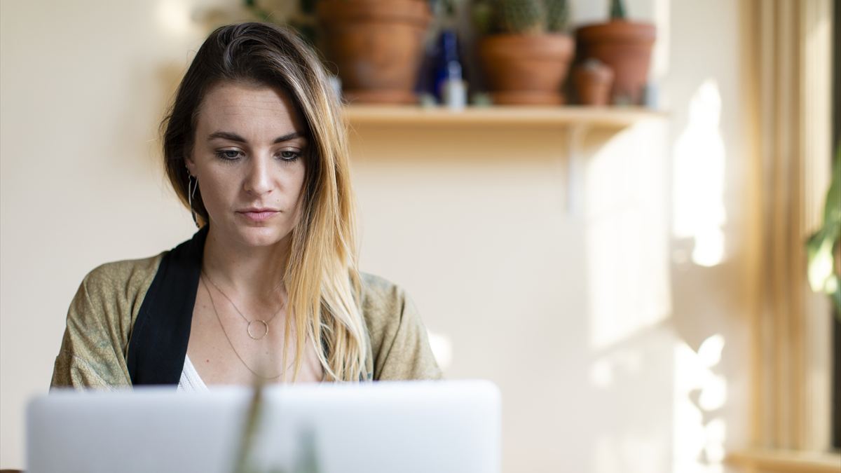 Mulher lendo com atenção a tela do notebook, sentada em casa