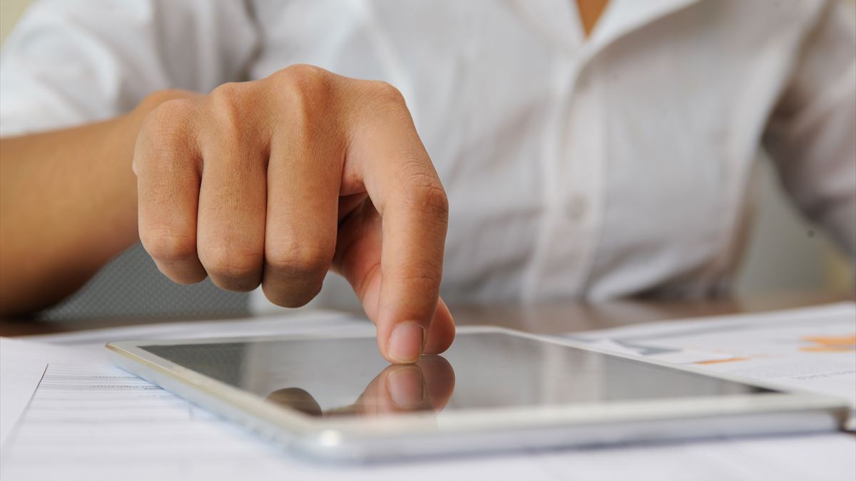 Dedo tocando a tela de um tablet sobre a mesa