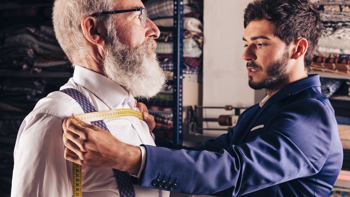 Alfaiate tirando as medidas de um cliente no ateliê